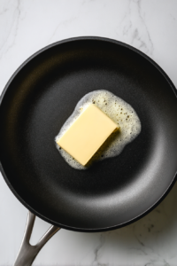 butter-melting-in-black-skillet-on-white-marble-stovetop