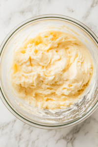 This image shows buttermilk and vanilla extract added to a custard batter in a glass bowl over a clean white marble countertop.