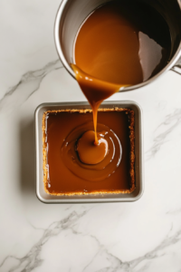 caramel-being-poured-over-shortbread-layer-in-pan-white-marble