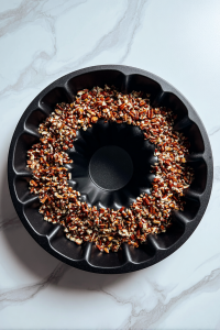 chopped-pecans-lined-evenly-in-black-bundt-pan-on-white-marble