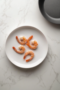 cooked-shrimp-resting-on-white-plate-near-cooktop