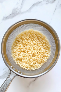 cooled_couscous_in_fine_mesh_strainer_over_white_marble_countertop-2