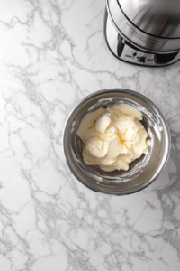 This image shows softened butter being creamed in a stand mixer bowl, with the sugar and cocoa mixture gradually added.