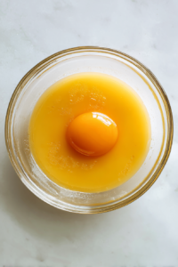 eggs-sugar-oil-vanilla-being-mixed-in-glass-bowl-on-white-marble