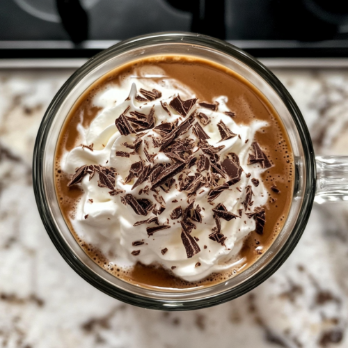 This image shows two glass mugs of Irish Mocha Latte topped with whipped cream and chocolate shavings, resting on a clean white marble countertop.