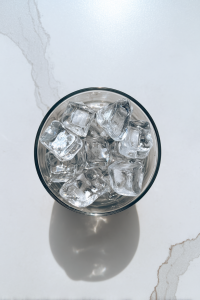 filling-clear-glass-with-ice-cubes-on-white-marble
