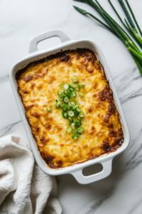 This image shows the golden-baked chicken casserole topped with fresh green scallions, on a clean white marble background.