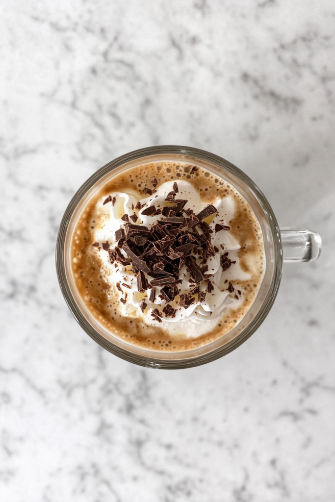This image shows a glass mug on a white marble cooktop filled with Irish Mocha Latte and topped with whipped cream and chocolate shavings.
