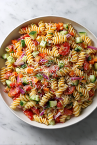 fully-mixed-pasta-salad-in-glass-bowl-on-marble