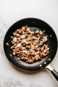 garlic-sauteing-with-sausage-in-black-skillet-on-marble