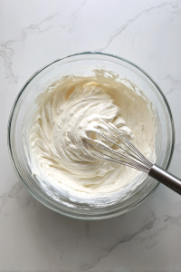 gently-whisking-heavy-cream-into-cheesecake-batter-in-clear-glass-bowl