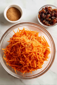 grated-carrots-brown-sugar-and-raisins-mixed-in-glass-bowl-on-marble