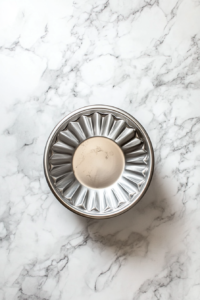 greasing-metal-bundt-pan-with-cooking-spray-on-white-marble