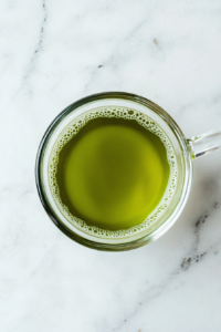 This image shows a minimalist top-down shot of a ceramic cup filled with rich green Japanese Mounjaro tea, set against a clean white marble background with no distractions.