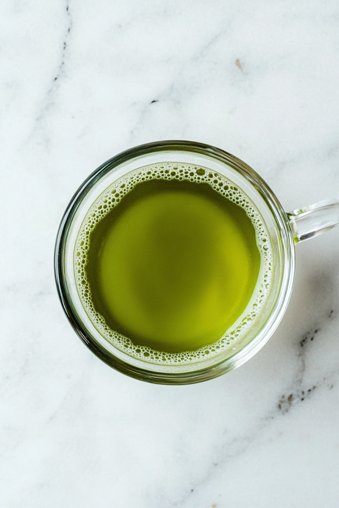 This image shows a minimalist top-down shot of a ceramic cup filled with rich green Japanese Mounjaro tea, set against a clean white marble background with no distractions.