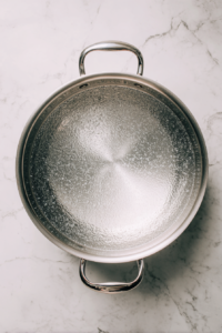 large-stainless-pot-boiling-salted-water-on-white-marble