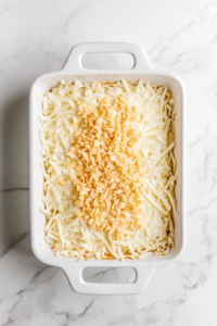 This image shows shredded mozzarella and buttery cracker topping added on top of the chicken mixture in a baking dish.