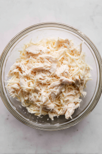 mixing-shredded-chicken-cream-cheese-garlic-powder-in-glass-bowl