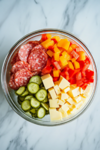 partially-layered-jar-with-cheese-salami-pickles-and-peppers-on-white-marble
