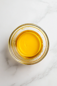 This image shows a glass bowl with half-melted unsalted butter sitting on a white marble cooktop, ready to be fully melted.