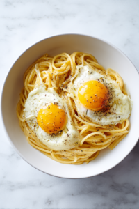 pasta-tossed-with-eggs-in-white-bowl-on-marble-counter