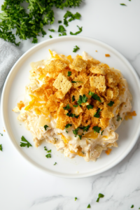 This image shows a portion of the chicken casserole served on a white plate next to the main baking dish, revealing its creamy, cheesy interior.