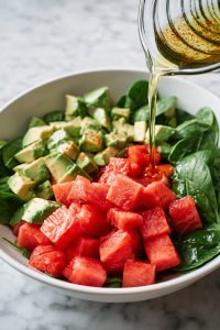 pouring-homemade-dressing-over-watermelon-avocado-spinach-salad