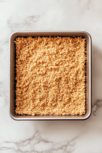 pressed-shortbread-layer-in-lined-baking-pan-on-white-marble