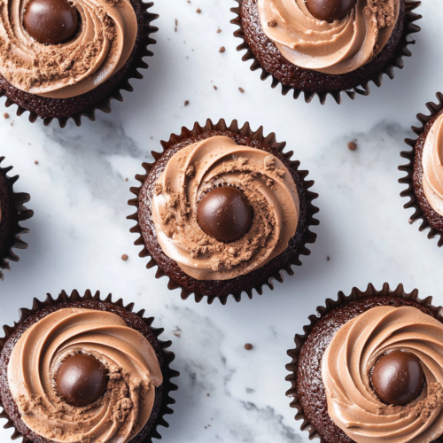 This image shows six decadent chocolate mocha cupcakes arranged on a white ceramic plate over a clean marble surface. Each cupcake is elegantly topped with swirled mocha frosting, a glossy ganache center, a chocolate-covered espresso bean, and a light dusting of cocoa.
