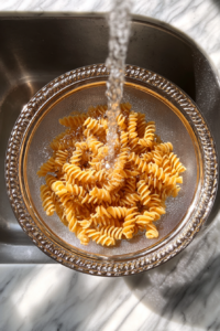 rinsing-cooked-pasta-in-clear-glass-colander-over-marble