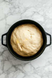 risen-dough-in-greased-black-dutch-oven-on-white-marble