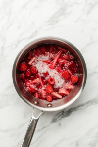 saucepan-simmering-rhubarb-raspberries-sugar-on-marble-counter