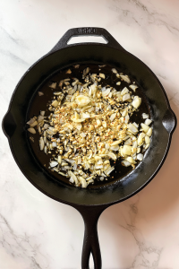 sauteing-aromatics-in-black-skillet-on-white-marble