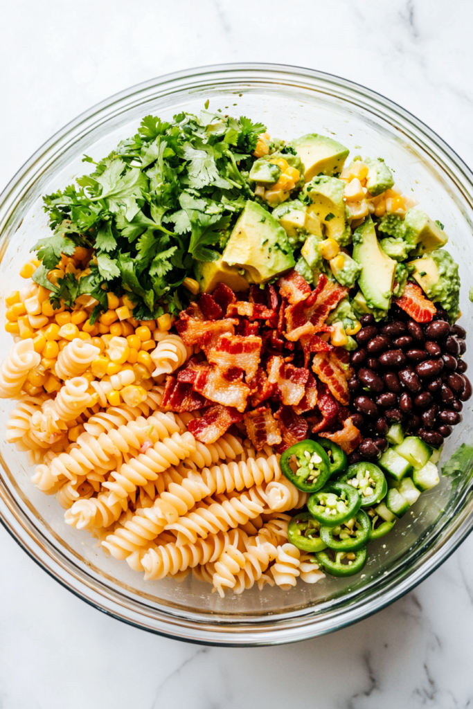 This image shows a serving of Mexican Street Corn Pasta Salad on a white ceramic plate with the salad bowl slightly visible in the background, all on a clean white marble surface.