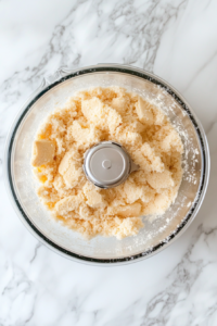 shortbread-cookies-being-pulsed-in-glass-food-processor-on-white-marble