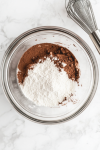 This image shows a top-down view of a metal cupcake pan lined with white paper liners on a white marble surface, with an oven preheating to 350°F in the background.