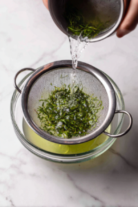 straining-mint-syrup-into-glass-bowl-over-white-marble