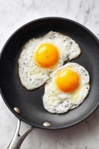 sunny-side-up-eggs-cooking-in-black-skillet-on-marble