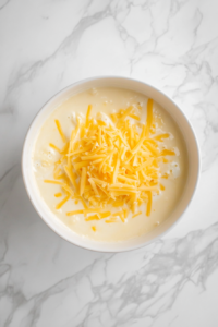 top-down-adding-cheddar-cheese-to-cream-sauce-in-black-dutch-oven