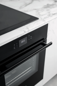 top-down-black-oven-door-slightly-ajar-on-white-marble-cooktop-background