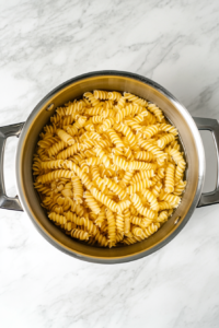 top-down-boiling-spiral-pasta-in-silver-pot-over-white-marble-cooktop