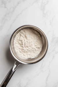 top-down-glass-saucepan-with-flour-cooking-in-melted-coconut-oil-on-white-marble