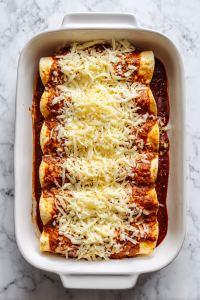 topping-white-chicken-enchiladas-with-shredded-cheese-in-white-dish