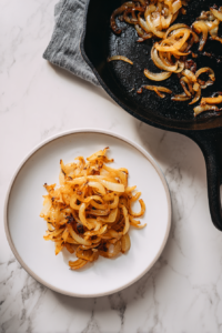 transferring-onions-to-white-plate-black-skillet-on-white-marble