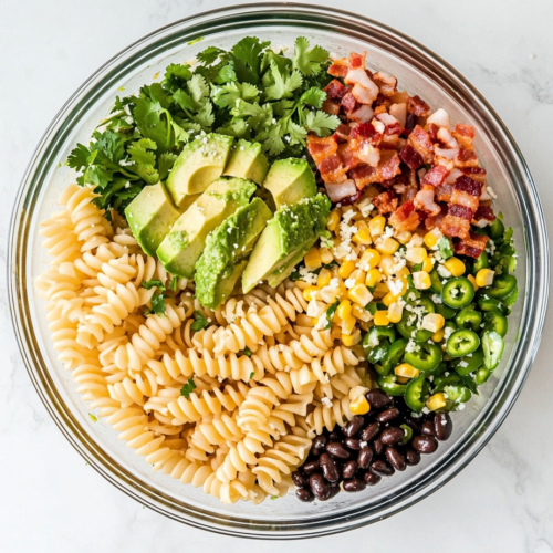 This image shows a top-down view of vibrant Mexican Street Corn Pasta Salad served in a clear glass bowl, resting on a clean white marble surface.