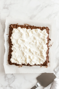 This image shows a chocolate Swiss roll log with a rich brown outer layer, rolled tightly on parchment paper on a white marble countertop.