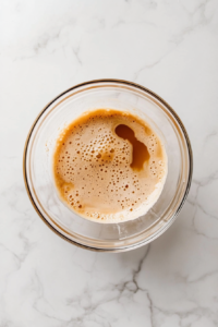 This image shows sifted dry ingredients in a large clear glass bowl, including flour, sugar, cocoa powder, baking soda, baking powder, salt, and espresso powder, ready for mixing.