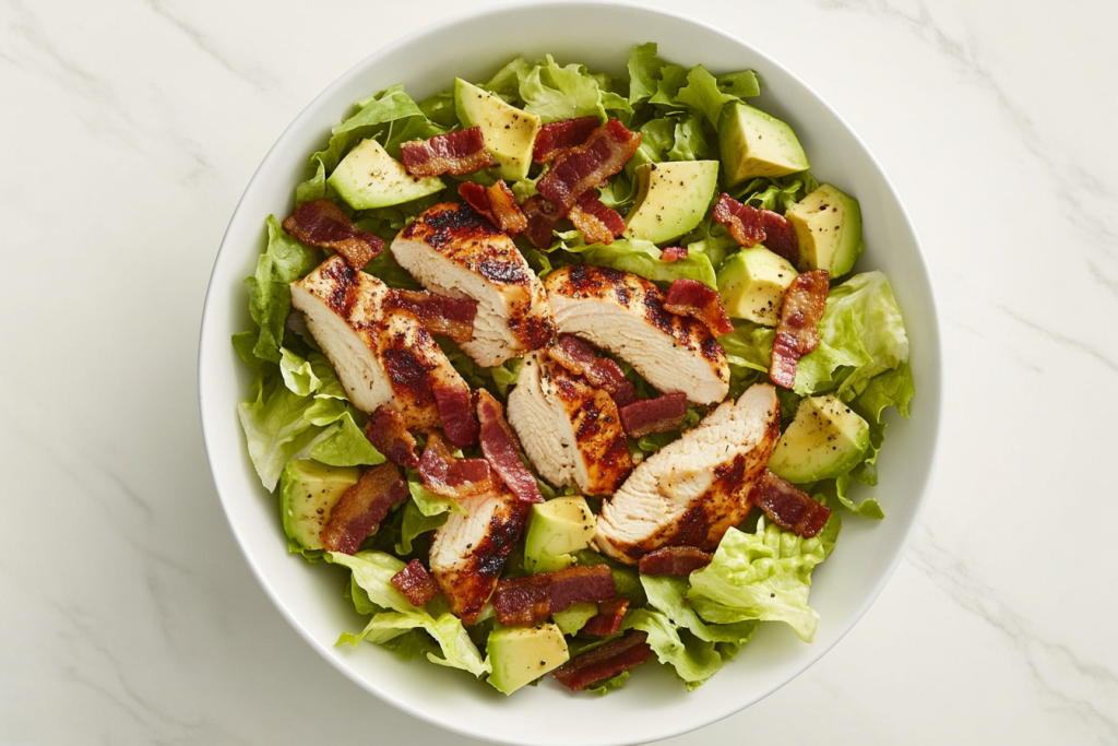 This image shows a vibrant chopped salad in a white bowl, featuring crispy bacon, grilled chicken, and a creamy dressing made with blue cheese, white wine vinegar, water, and pepper, blended to perfection.