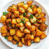 This image shows a plate of crispy, golden-brown breakfast potatoes garnished with freshly chopped cilantro. The potatoes are perfectly fried to a crunchy texture with a soft interior, making for a delicious and savory morning dish.